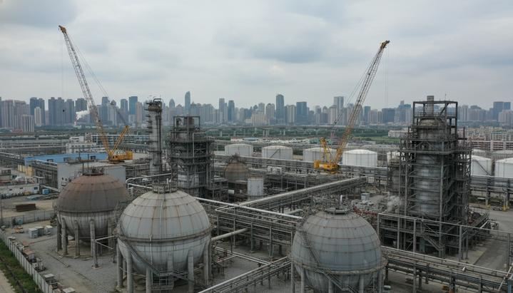 Промышленный пейзаж: никель-кобальтовый завод в процессе модернизации, с резервуарами, трубами и строительными лесами на фоне города.