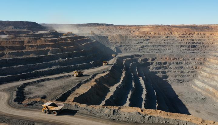 Thiess продлила контракт с MACH Energy на руднике Mount Pleasant до 2031 года Панорамный вид на огромный угольный карьер с высоты. Большие карьерные самосвалы движутся по многоуровневым террасам разреза.